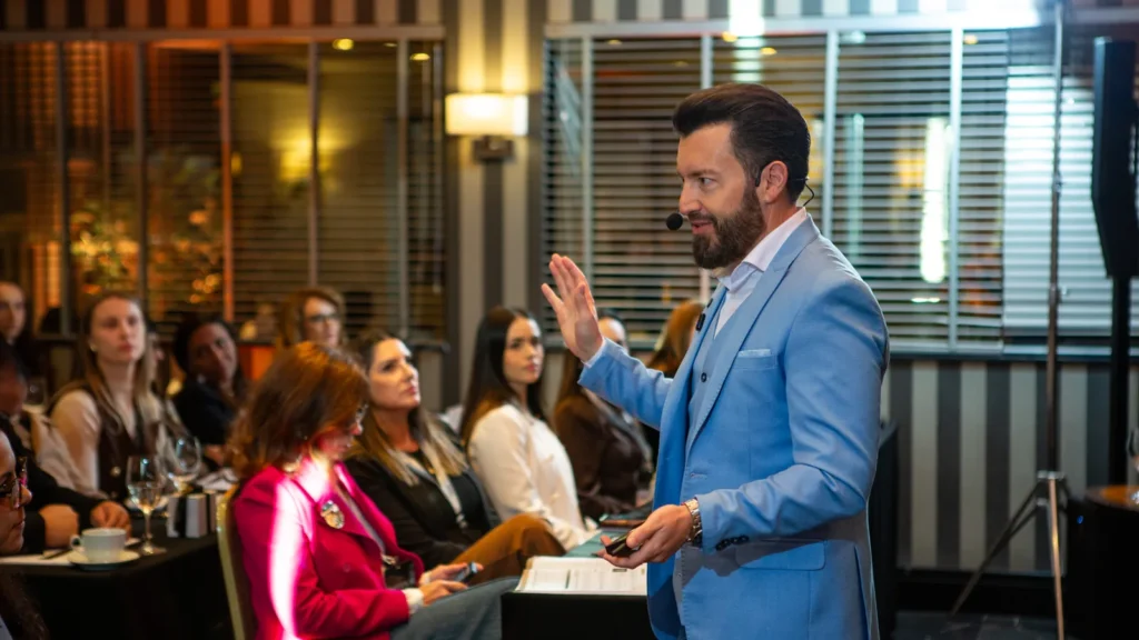 O que é high ticket na prática: Eduardo Arruda ensina em pé para participantes sentados em uma sala de imersão
